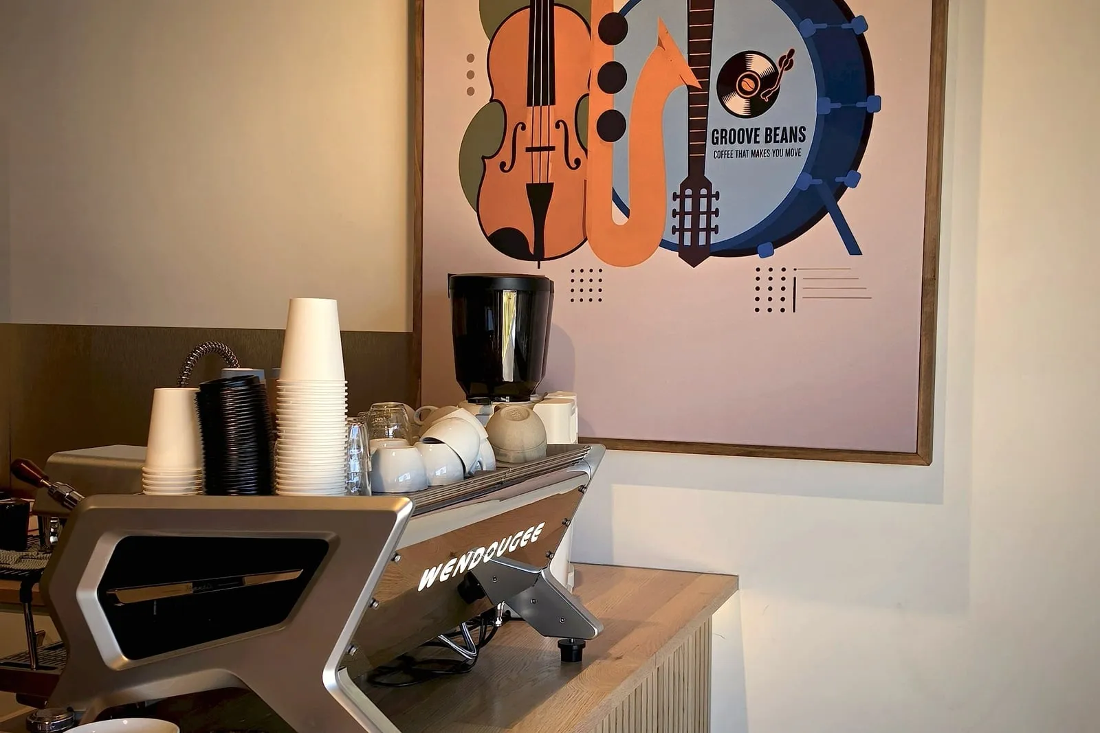 Espresso machine stacked with cups on the oak counter, in front of the Groove Beans instruments mural