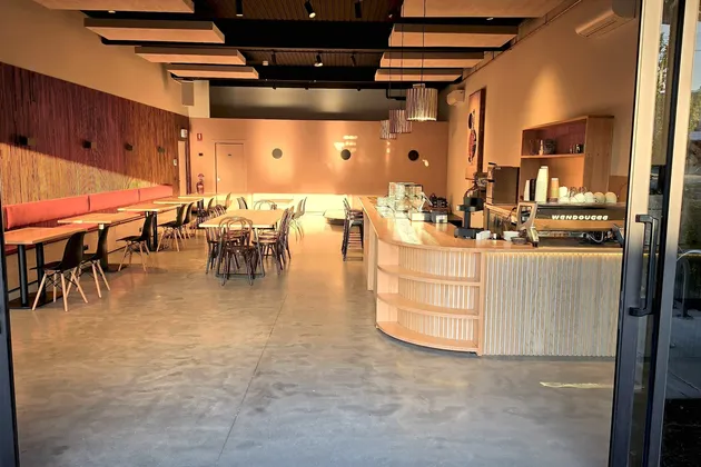 The cafe seen from the open front doors in warm morning light, with red booths along the walnut slat wall and the curved oak counter