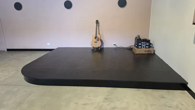 The small black stage with an acoustic guitar on a stand